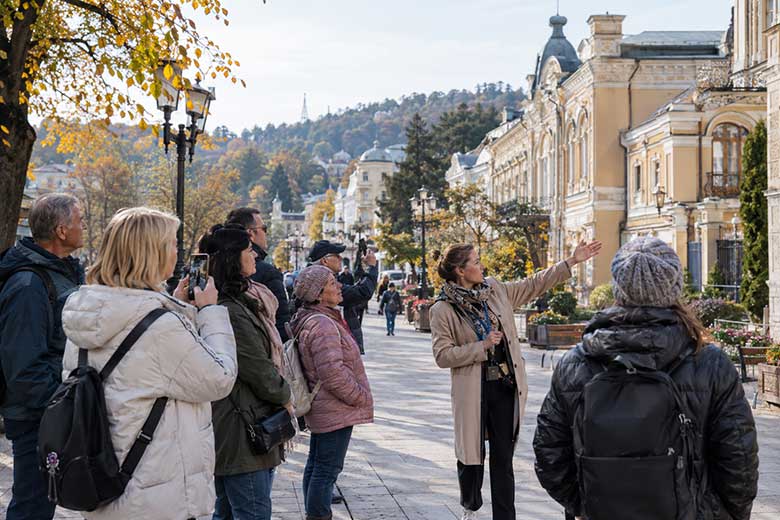 Группа туристов с экскурсоводом гуляет по Курортному бульвару Кисловодска, рассматривает историческую архитектуру и фотографирует достопримечательности.